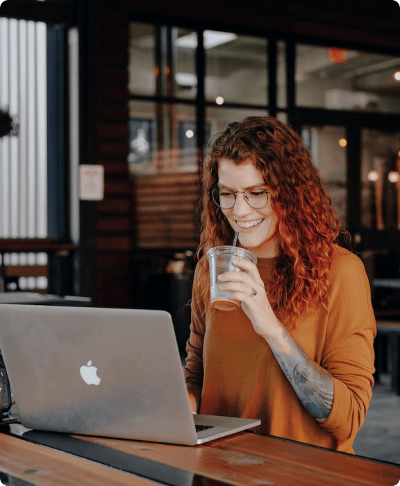 Woman standing in front of a laptop, drinking an iced coffee through a straw.